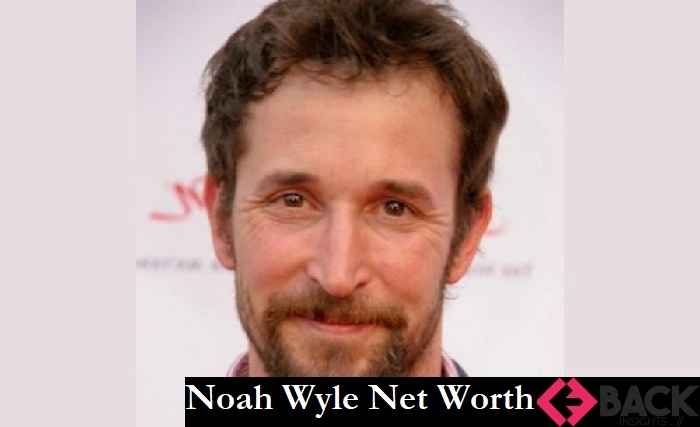 Noah Wyle stands confidently in a suit, reflecting his estimated net worth and successful career from ER to present day.